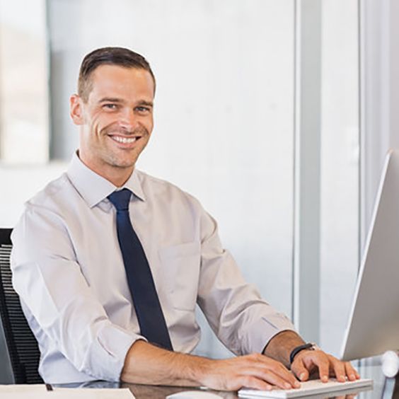 Portrait of confident manager sitting at desk and looking at camera. Portrait of smiling business man working at computer. Successful formal man in his new modern office.